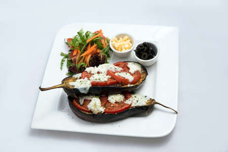 A low contrast warm Hero shot of a main course platter with grilled aubergine with buffalo cheese, tomato, olives & vegetables on the side, on a minimal white background with a 45 degree angle from diagonal perspective.の写真素材