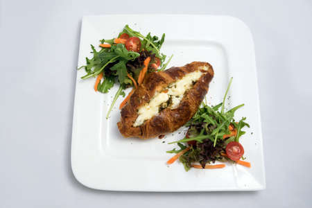 A low contrast Hero shot of a breakfast platter with cheese and zaatar filled croissant with vegetables- carrot, tomato, lettuce on a minimal white background with a 30 degree angle from front perspectiveの写真素材