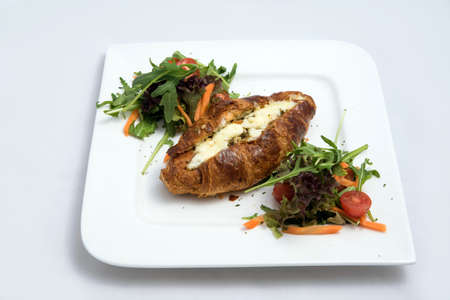 A low contrast Hero shot of a breakfast platter with cheese and zaatar filled croissant with vegetables- carrot, tomato, lettuce on a minimal white background with a 30 degree angle from front perspectiveの写真素材