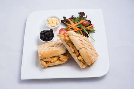 A low contrast Hero shot of a breakfast platter with grilled chicken panini sandwich with olives, cheese & vegetables- carrot, tomato, lettuce on a minimal white background with a 45 degree angle from almost front perspectiveの写真素材