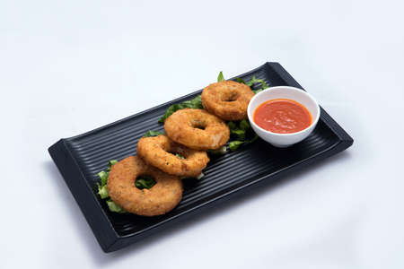 A low contrast Hero shot of an appetizer platter of onion rings with lettuce and tomato chutney on a minimal white background with a 45 degree angle front perspectiveの写真素材