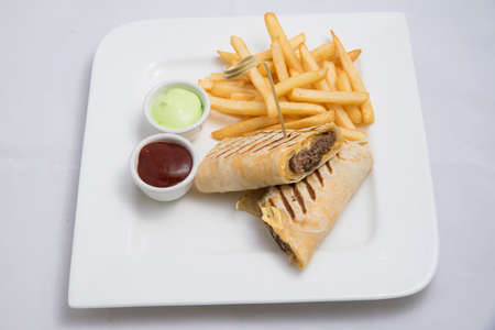 A low contrast Hero shot of a beef wrap sandwich with samurai & alger sauce and fries on the side, on a minimal white background with a 45 degree angle from front zoomed in perspectiveの写真素材