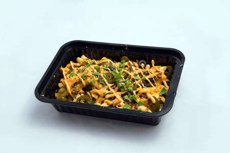 A high contrast Hero shot of a Take-Away Hot Loaded fries / chips with cheese, ground meat, olives, jalapeno, sauce & oregano, on a minimal white background with a 45 degree angle from zoomed out right diagonal perspective.の写真素材
