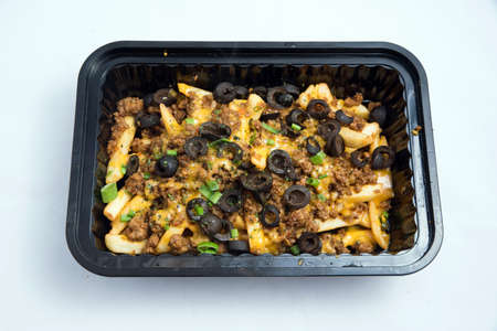 A high contrast Hero shot of a Take-Away Hot Loaded fries / chips with ground meat, olives, cheese, jalapeno, sauce & oregano, on a minimal white background with a 90 degree angle from zoomed  vertical perspective.の写真素材