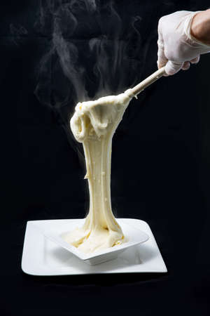 A high contrast artistic hero shot of fresh hot cheese being served on to a platter with smoke coming off the stretched cheese on a minimal white background from a flat horizontal perspectiveの写真素材