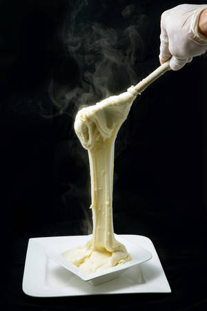 A warm artistic hero shot of fresh hot cheese being served on to a platter with smoke coming off the stretched cheese on a minimal white background from a flat horizontal perspectiveの写真素材