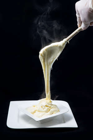 A low contrast artistic hero shot of fresh hot cheese being served on to a platter with smoke coming off the stretched cheese on a minimal white background from a flat horizontal perspectiveの写真素材