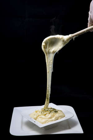 A high contrast artistic hero shot of fresh hot cheese being served on to a platter with sprinkled oregano on a minimal white background from a flat horizontal perspectiveの写真素材