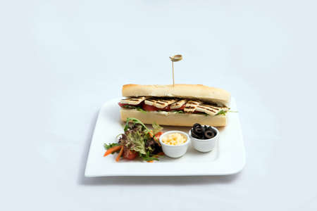 A high contrast Hero shot of a Grilled Halloumi cheese baguette with olives & salad on the side, on a minimal white background with a 45 degree angle from frontal zoomed out perspectiveの写真素材