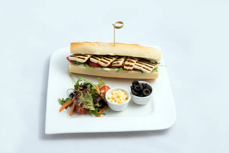 A high contrast Hero shot of a Grilled Halloumi cheese baguette with olives & salad on the side, on a minimal white background with a 60 degree angle from frontal zoomed perspectiveの写真素材