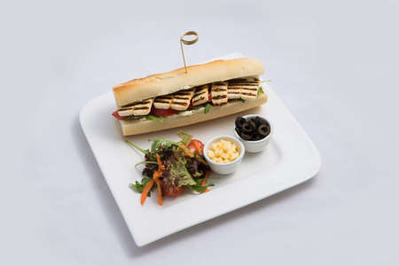 A low contrast Hero shot of a Grilled Halloumi cheese baguette with olives & salad on the side, on a minimal white background with a 60 degree angle from diagonal zoomed perspectiveの写真素材
