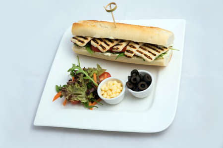 A high contrast Hero shot of a Grilled Halloumi cheese baguette with olives & salad on the side, on a minimal white background with a 75 degree angle from slant zoomed perspectiveの写真素材