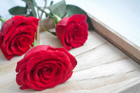 Close up of three red roses on a wooden tray creating romantic valentine's day atmosphereの写真素材