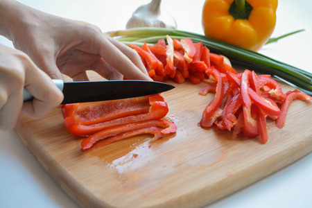 Female cook chopping fresh vegetables on wooden board: red and yellow bell pepper, green onions, chili, garlic, carrot and spinachの写真素材