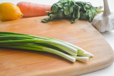Female cook chopping fresh vegetables on wooden board: red and yellow bell pepper, green onions, chili, garlic, carrot and spinachの写真素材
