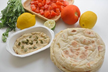 Hummus with pumpkin seeds sprinkled on top, pita bread, chopped tomatoes, lemon, lime and arugula