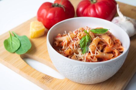 Classic italian penne pasta arrabbiata with its ingredients in the background: fresh tomatoes,...