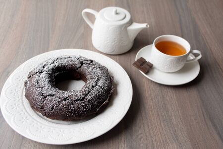 Chocolate cake with a hole in the center and sugar powder sprinkled on top, on the background are a teapot and tea cup with teaの写真素材