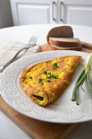 Fluffy breakfast omelette with green spring onions and fresh toast bread on a wooden surface with a napkin and metal forkの写真素材