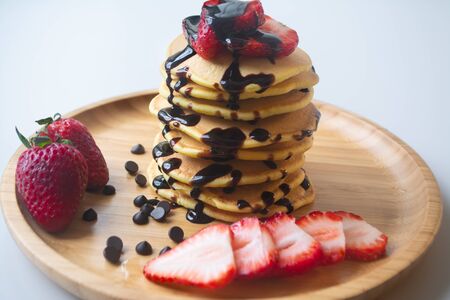 Fluffy breakfast pancakes with chocolate syrup, chocolate chips and fresh ripe strawberries served...