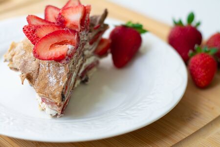 Light summer dessert: a slice of crepe layer cake with whipped cream, chocolate chips and strawberries between the layers. It is decorated with strawberries and placed on a white plate.の写真素材