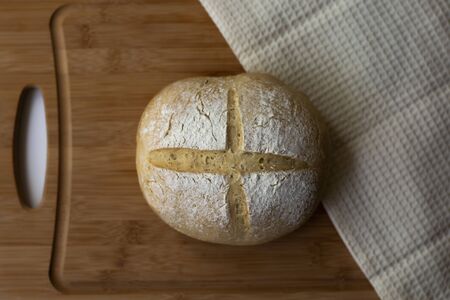 A loaf of homemade sourdough yeast bread boule with a simple cross style scoring technique on a...