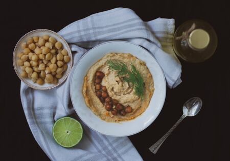 Chickpea vegan hummus garnished with dill and baked chickpeas on black background with vintage...