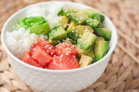 Hawaiian poke bowl with smoked salmon lox, avocado, white rice, cucumber and sesame seeds. Bright...