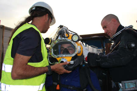 Photo of a diver who is willing to dive - he is dressed in a suit and helmet. Workers helps him