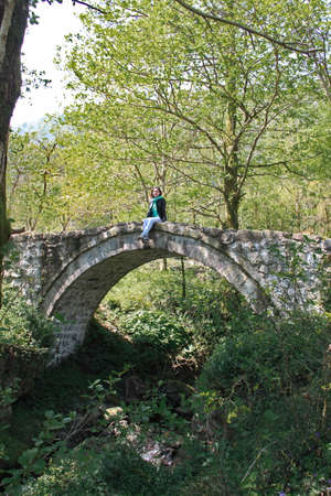 A girl stands on an old antique bridge in the forest, Georgia, village of Mirvetiの写真素材