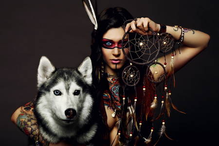 Beautiful woman in native american costume posing in a studio with hasky dogの写真素材