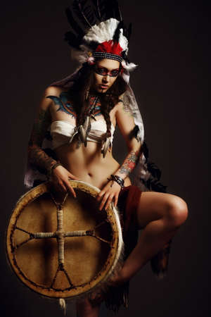 Beautiful woman in native american costume with roach on her head posing in a studioの写真素材
