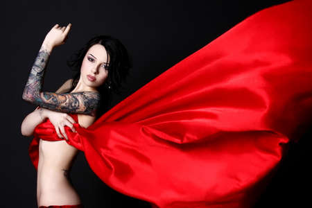 Beautiful girl with tattoos with a red cloth on a black backgroundの写真素材