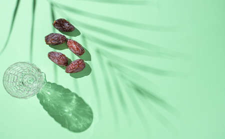 Creative Ramadan Kareem greeting card. A glass of water and five fresh dates with the shade of a...