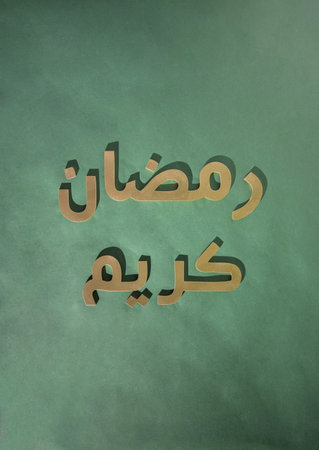 Ramadan Kareem greeting message: "May the month of Ramadan be blessed to you!" Golden arabic 3d letters with shadows on a dark green background. Flat lay creative minimal design.の写真素材