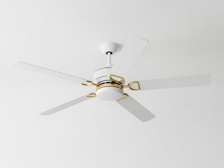 A modern white ceiling fan with five blades and elegant gold detailing is suspended from a white ceiling, providing a clean and contemporary aesthetic for home cooling.の写真素材