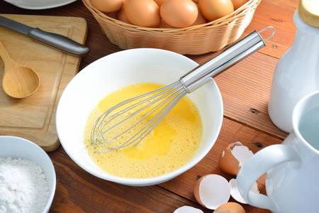 eggs yolk with whisk on wooden table