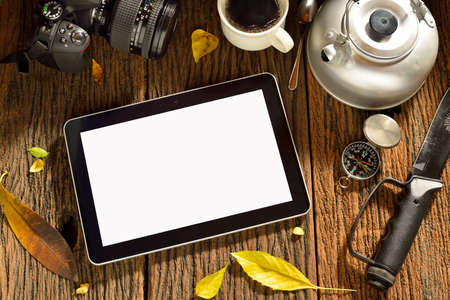 Tablet computer and camping equipment on old wooden tableの写真素材