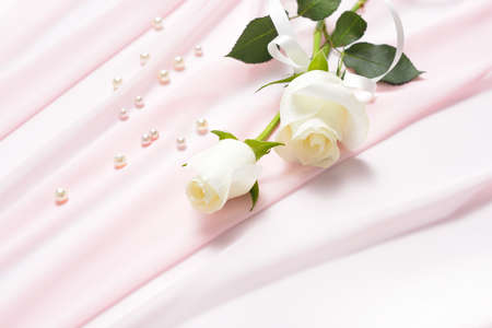 White rose flowers tied with ribbon on pink cloth with pearlsの写真素材