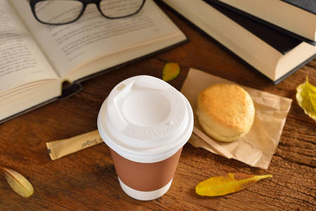 Paper cup of coffee with pastry and books on wooden tableの写真素材