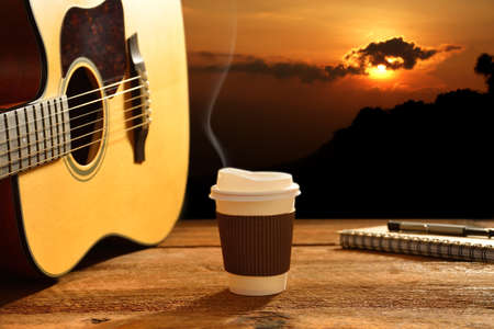 Paper cup of coffee and guitar with the sun in backgroundの写真素材