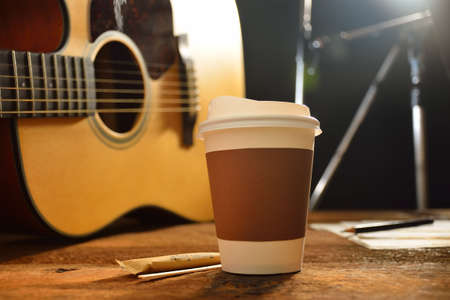 Paper cup of coffee and guitar on wooden tableの写真素材