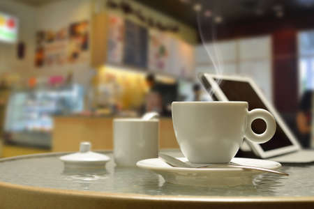 Cup of coffee with smoke and tablet computer in coffee shopの写真素材