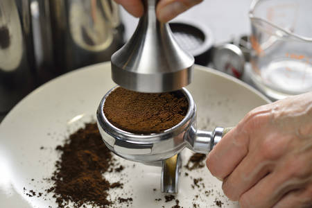 Barista using a tamper to press ground coffee into a portafilterの写真素材