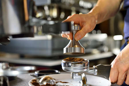 Barista using a tamper to press ground coffee into a portafilterの写真素材