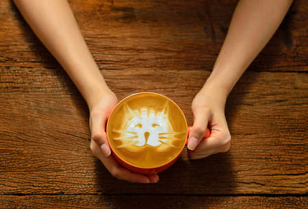Woman holding cup of coffee latte on wooden tableの写真素材