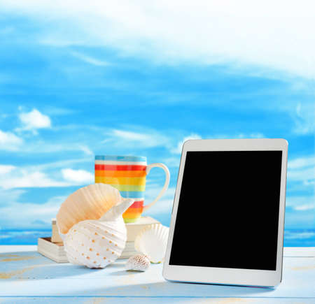 Tablet computer and seashells on the beach with blue sea and skyの写真素材