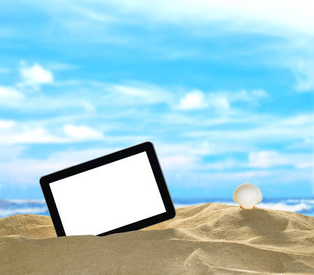 Tablet computer and seashells on the beach with blue sea and skyの写真素材