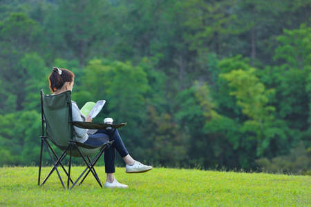 Young woman sitting on camping chair reading a book in the parkの写真素材