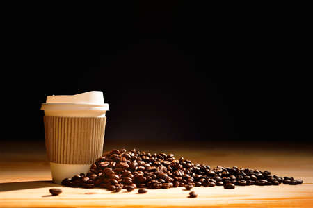 Paper cup of coffee and coffee beans on wooden tableの写真素材
